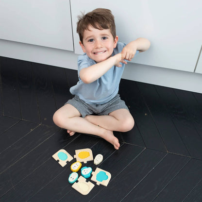 A young child sitting on a dark wood floor playing with the wooden animal puzzle pieces arranged around them.