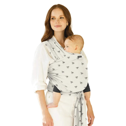 Moby Classic Baby Wrap in a light fabric with small bow motifs shown in a front-carry position, with a parent holding a baby close and the wrap tied securely.