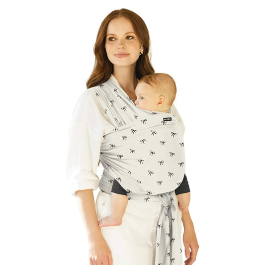 Moby Classic Baby Wrap in a light fabric with small bow motifs shown in a front-carry position, with a parent holding a baby close and the wrap tied securely.