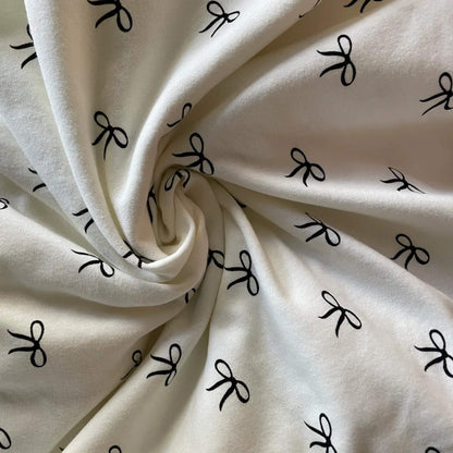 Swirled section of light fabric printed with small black bows, showing texture and drape.