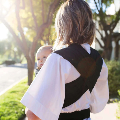Back view showing the cross-over straps of a black baby wrap tied securely around the waist.