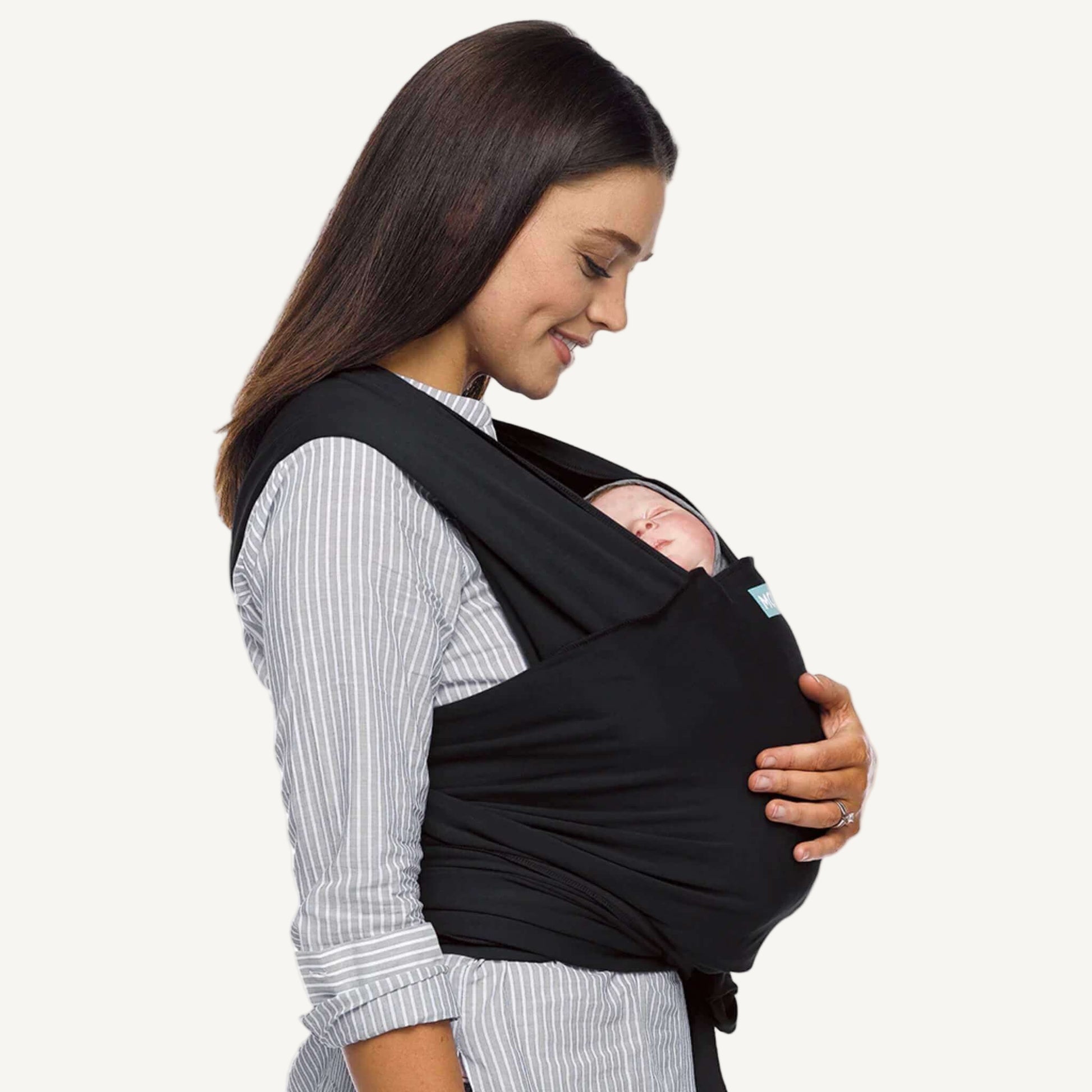 Mother looking down at her newborn baby resting in a black wrap carrier, side profile view.