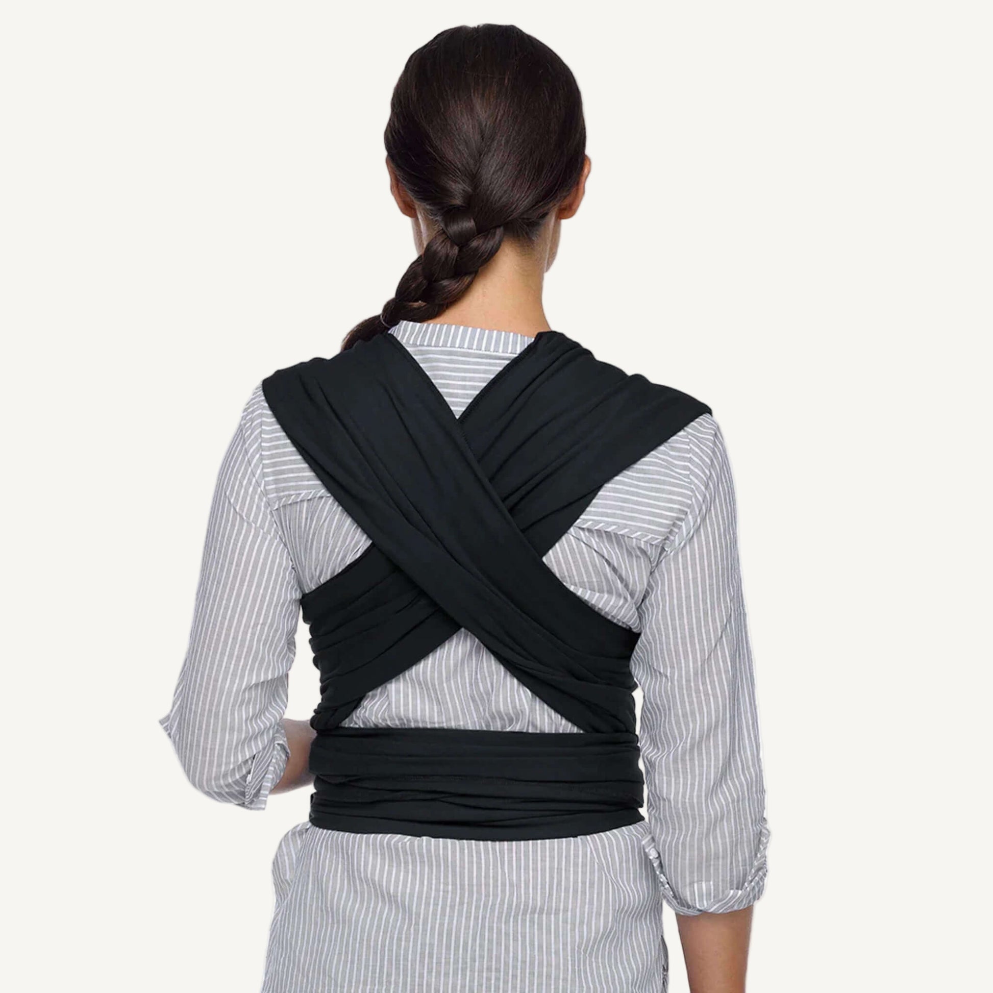 Woman outdoors holding her baby in a front carry using a black wrap carrier, surrounded by pink flowers.