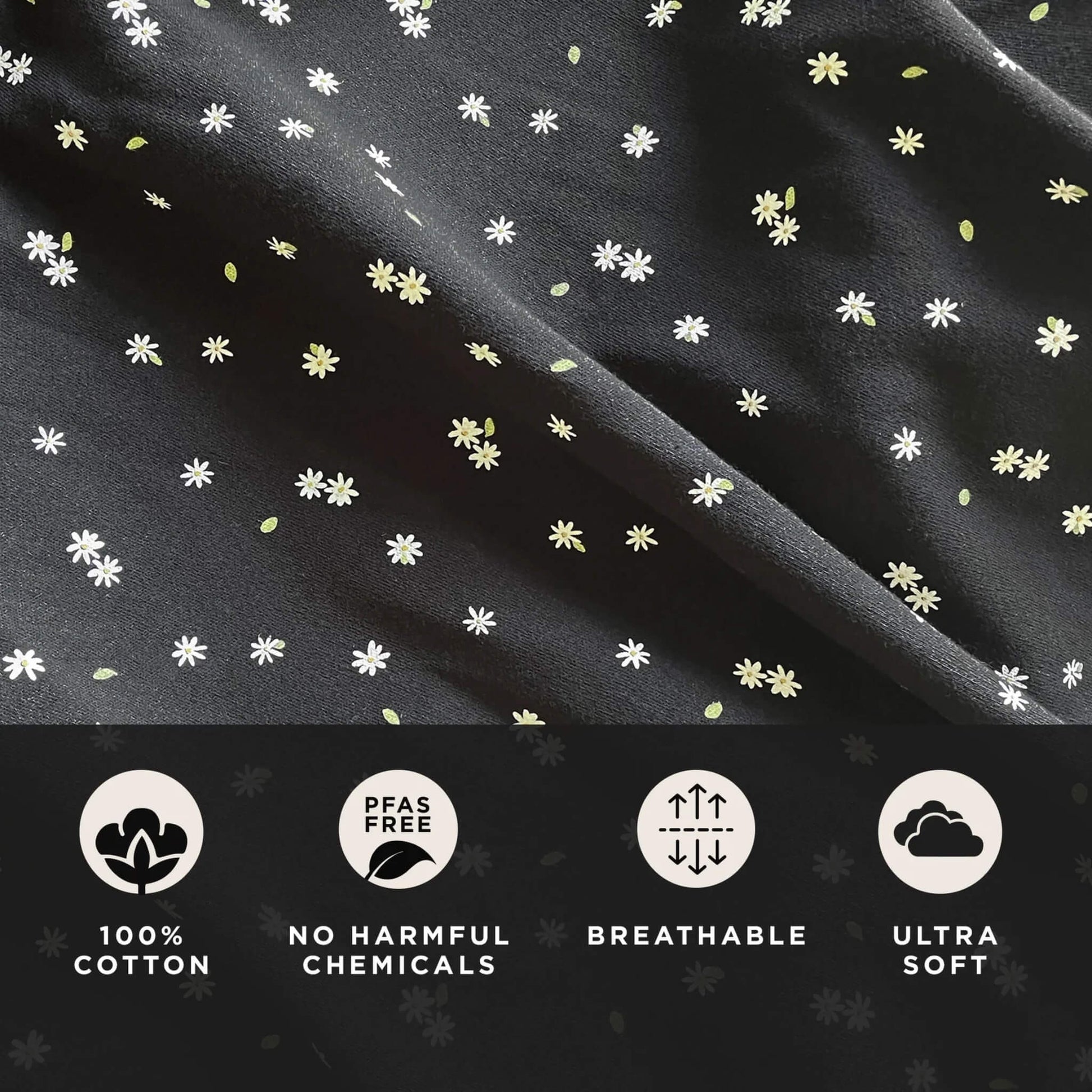 Close-up of black cotton fabric scattered with small white daisy motifs and light green leaf details, showing the soft texture and pattern clearly.