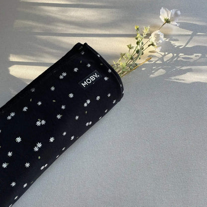Rolled black baby wrap decorated with tiny white daisies resting on a surface, with small flowers placed beside it in soft natural light.