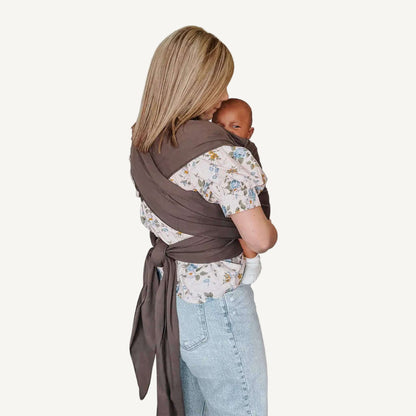 Mother viewed from the side showing the cross-over back design and tied ends of the Hickory brown baby wrap carrier.