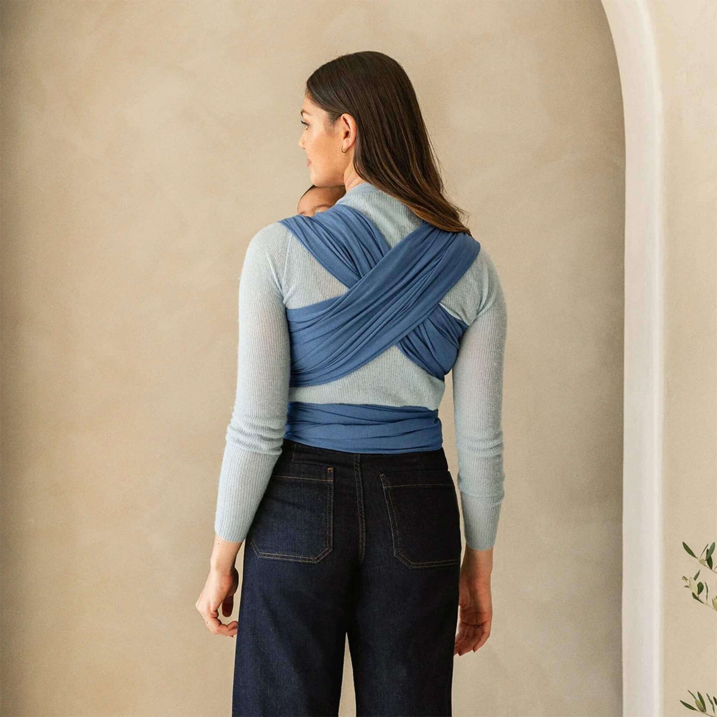 Mother showing the cross-over back design of the Ocean blue baby wrap while holding her baby.
