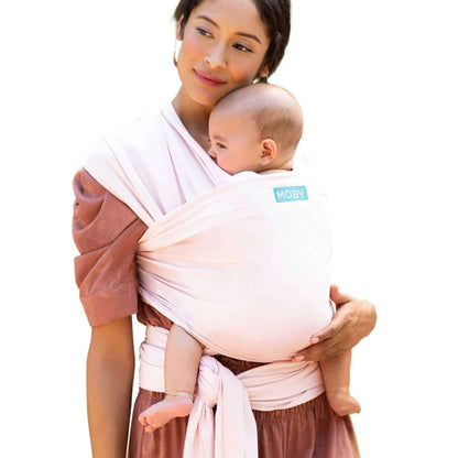 A mother wearing the Moby Classic Baby Wrap in Rose Quartz pink, holding her baby close against her chest.