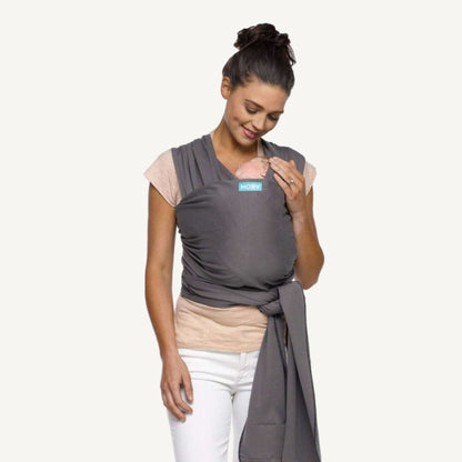Mother wearing a Slate grey baby wrap tied securely at the waist while holding her sleeping baby.