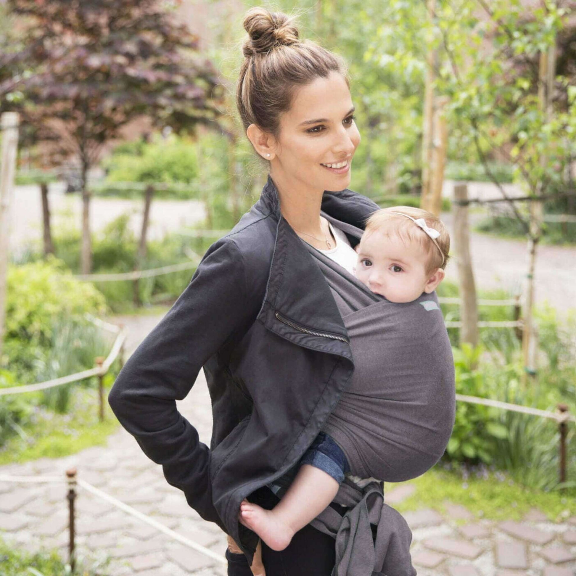 Mother walking outdoors wearing a Slate grey wrap carrier, holding her baby who looks out curiously.