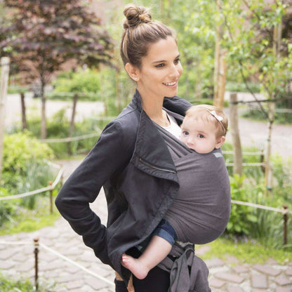 Mother walking outdoors wearing a Slate grey wrap carrier, holding her baby who looks out curiously.