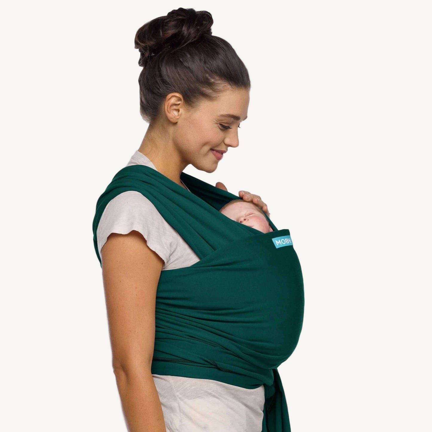 Mother viewed from the side carrying her sleeping baby in a Pacific green baby wrap carrier.