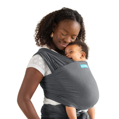 Moby Elements Baby Wrap in a deep grey shade shown in a front-carry position, with a parent holding a baby close and the fabric wrapped securely for support.