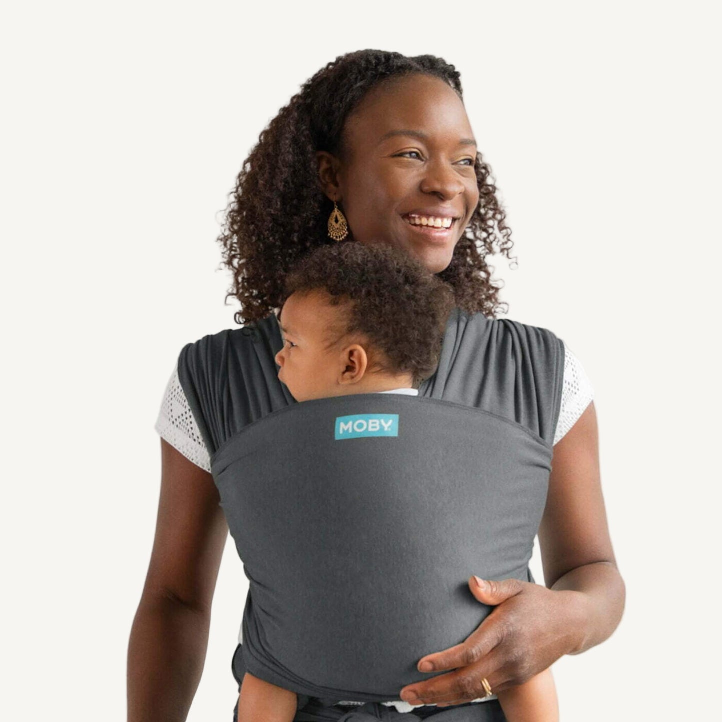 Parent carrying a baby in a deep grey wrap, with the baby resting against their chest and the fabric wrapped snugly around both.
