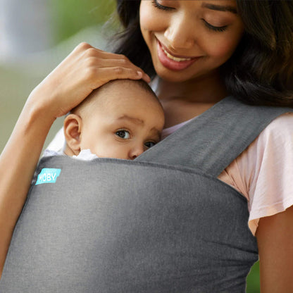 Baby resting against an adult’s chest in a deep grey wrap, with the adult’s hand gently placed on the baby’s head.