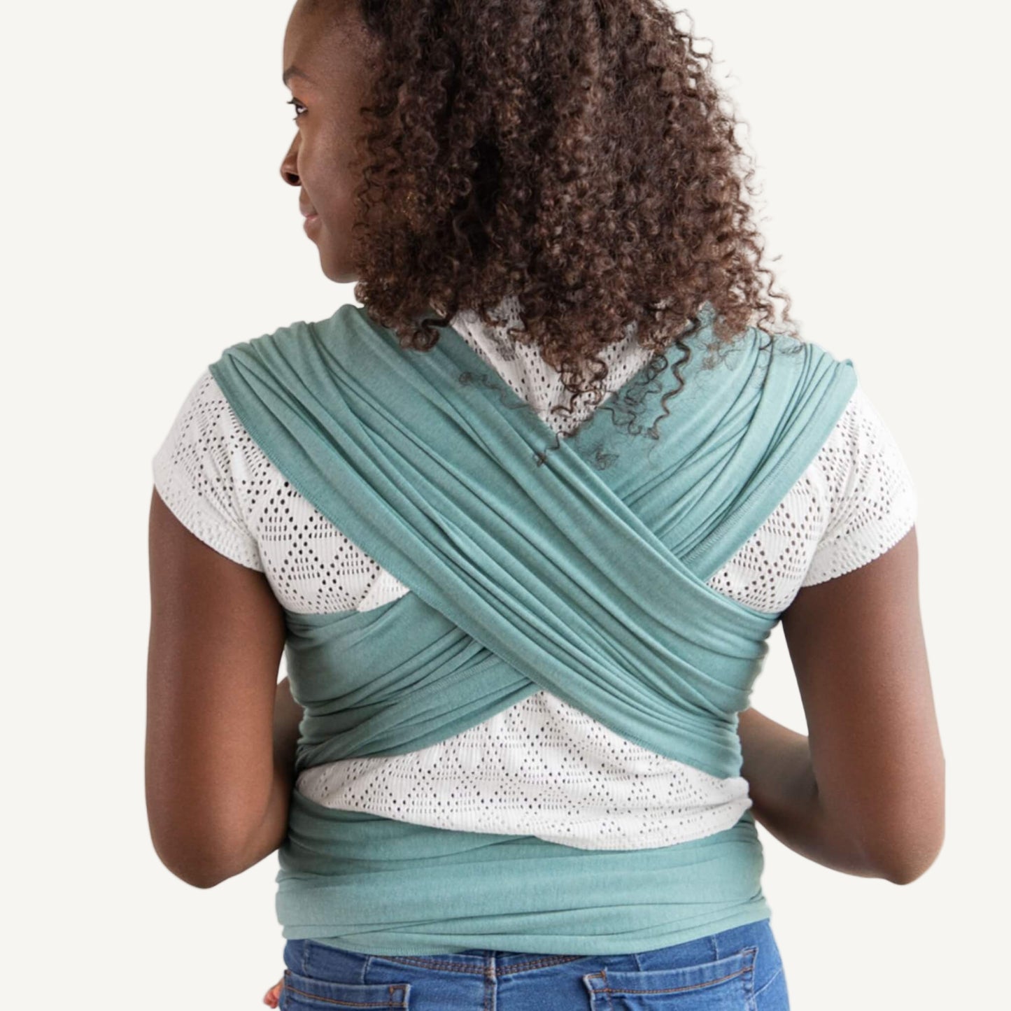 Wide teal wrap fabric crossed across a parent’s back, with the layers spread evenly for support and tied at the waist.
