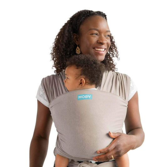 Moby Elements Baby Wrap in taupe shown with a parent carrying a baby securely in a front-carry position, fabric wrapped snugly around both for support.