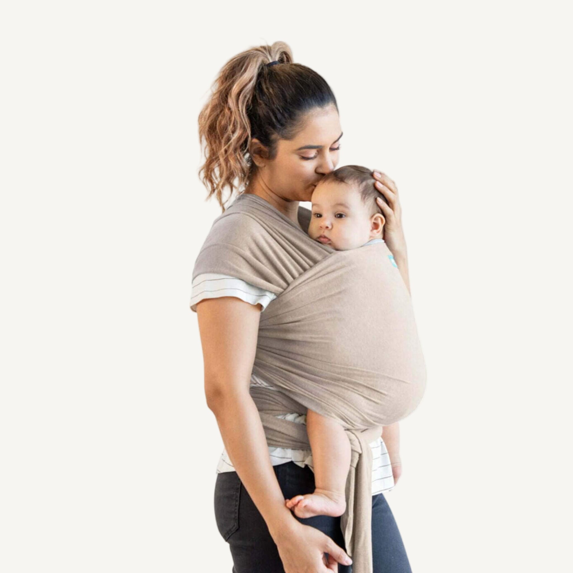 Parent standing with a baby in a front-carry position  held close against the chest in a soft taupe wrap, fabric tied neatly at the waist.