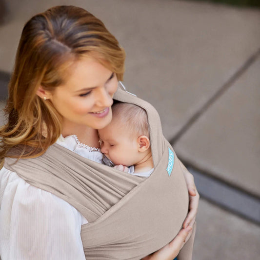 Sleeping newborn resting against a parent’s chest inside a soft taupe wrap, with the fabric gathered securely around the baby.