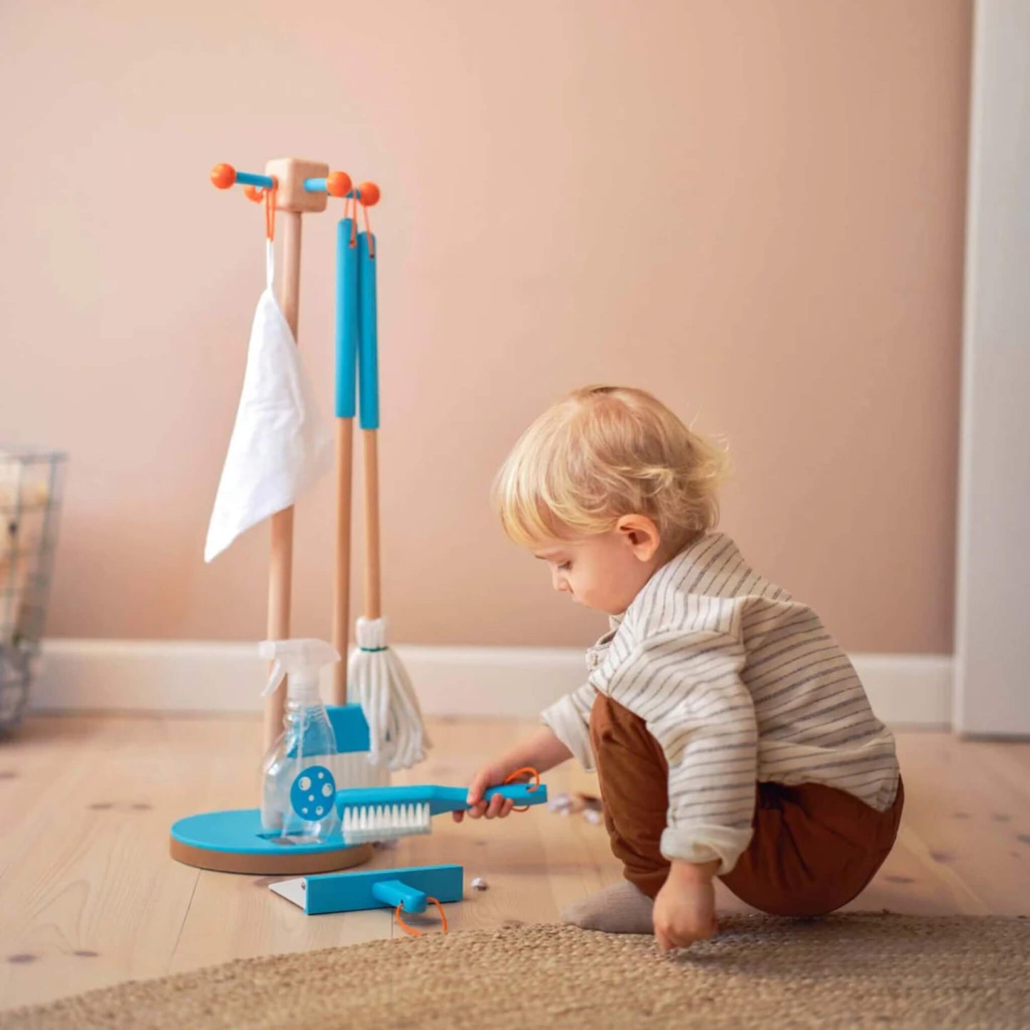 Toddler crouching with brush in hand, exploring the Moover Cleaning Set in a calm indoor setting.