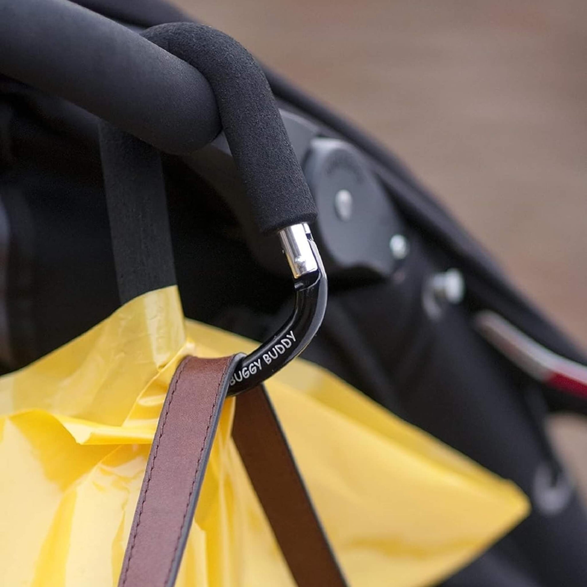 Pram handle with buggy clip in use, supporting shopping bags and a handbag.