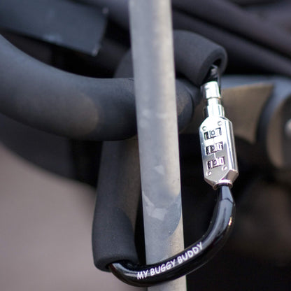 Foam-handled clip with combination lock connecting a pram handle and metal pole, shown indoors in soft lighting.