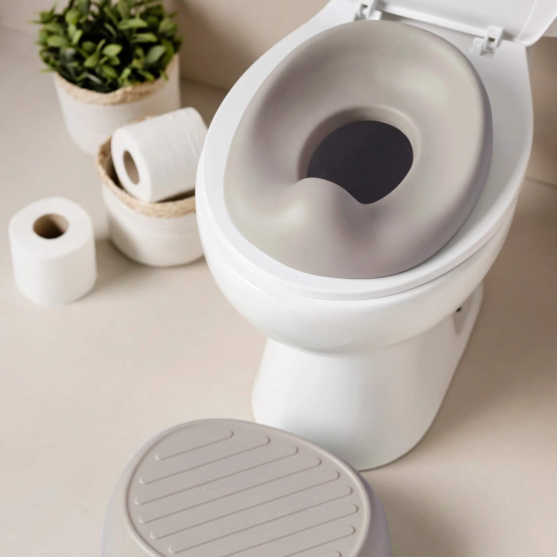 A cushioned potty seat placed on a standard toilet, with bathroom accessories visible in the background.
