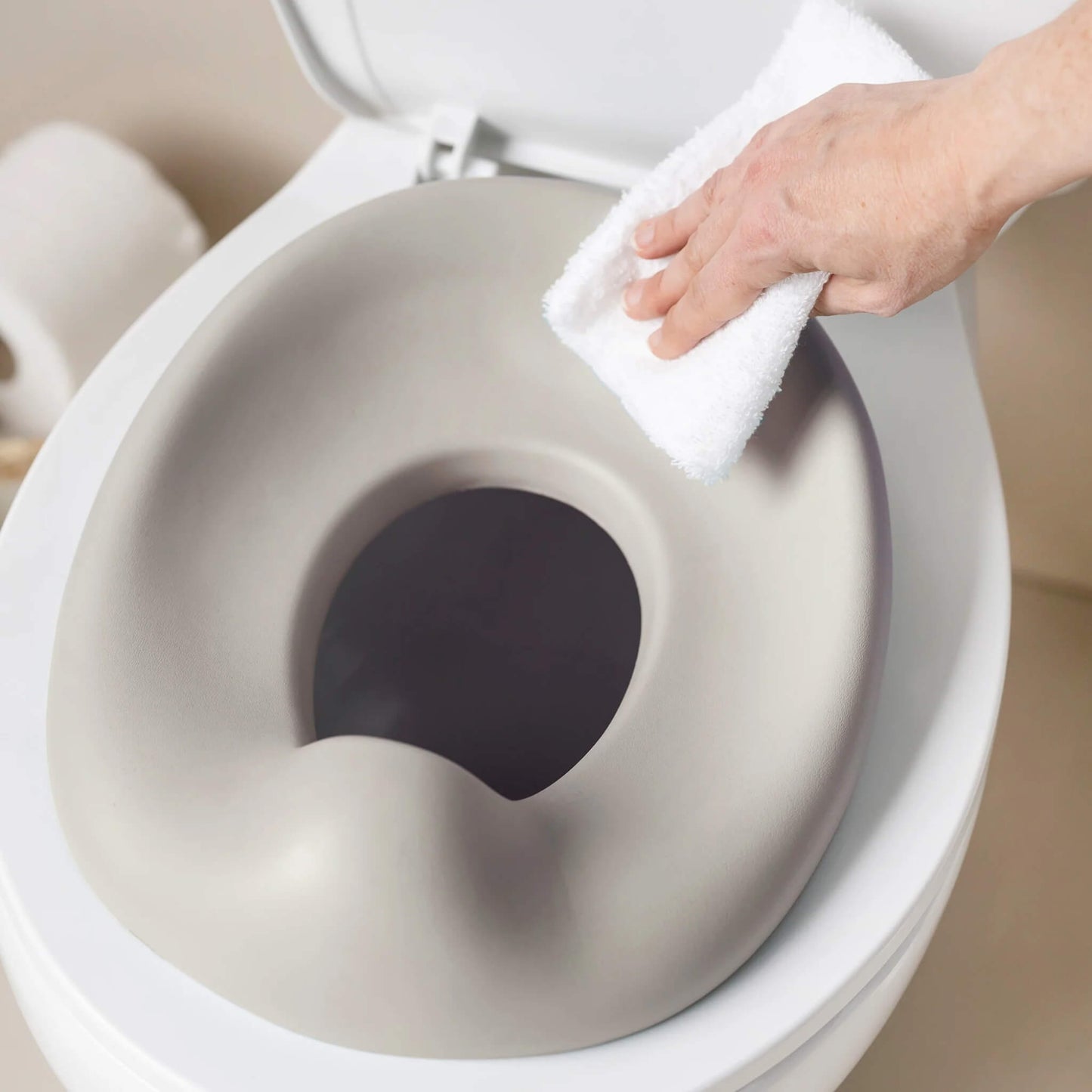 A hand wiping the potty seat while it sits on a toilet, highlighting the smooth, easy-clean surface.
