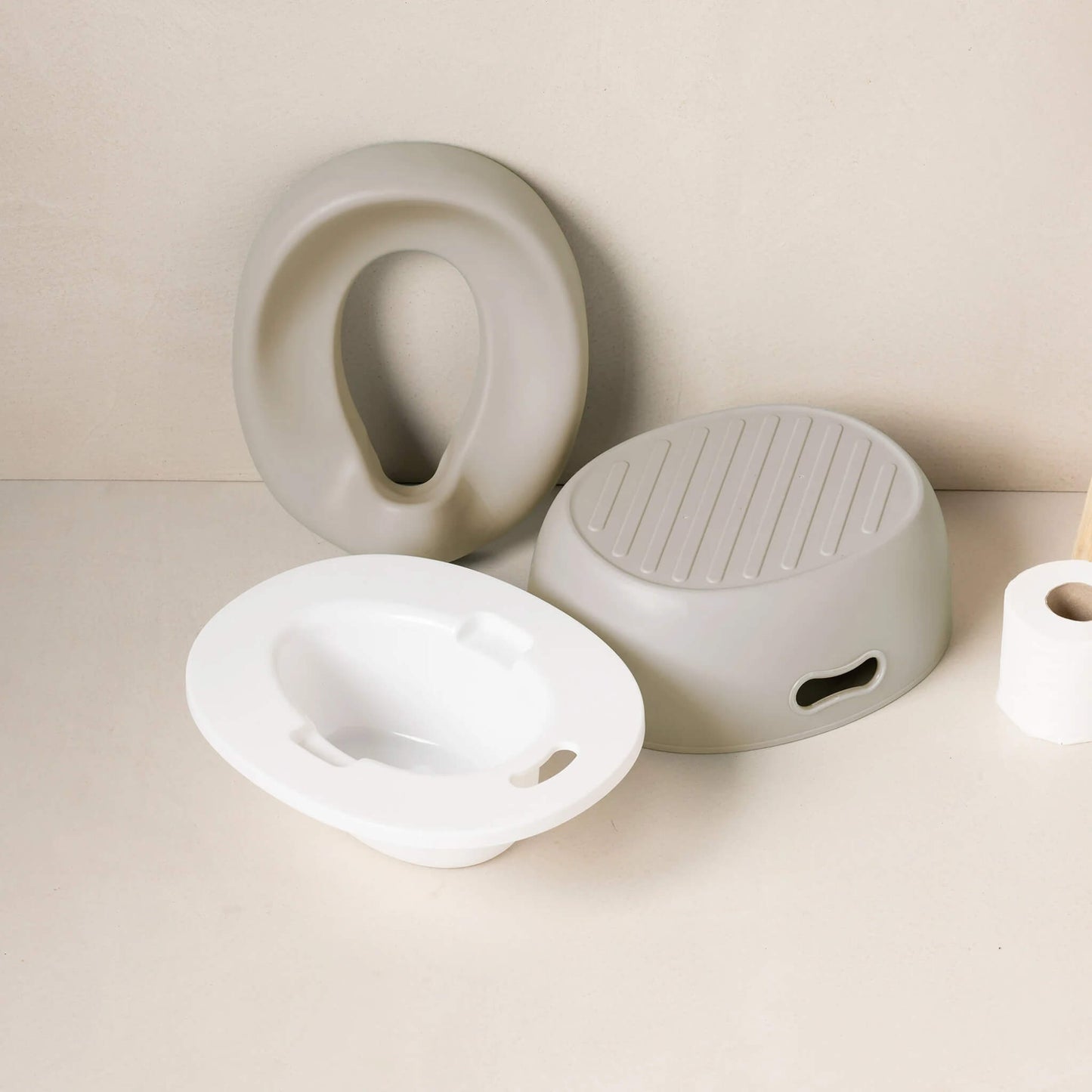 A set of potty components laid out on a bathroom surface, including a cushioned seat, an inner bowl, a flat white lid section and a small step stool.