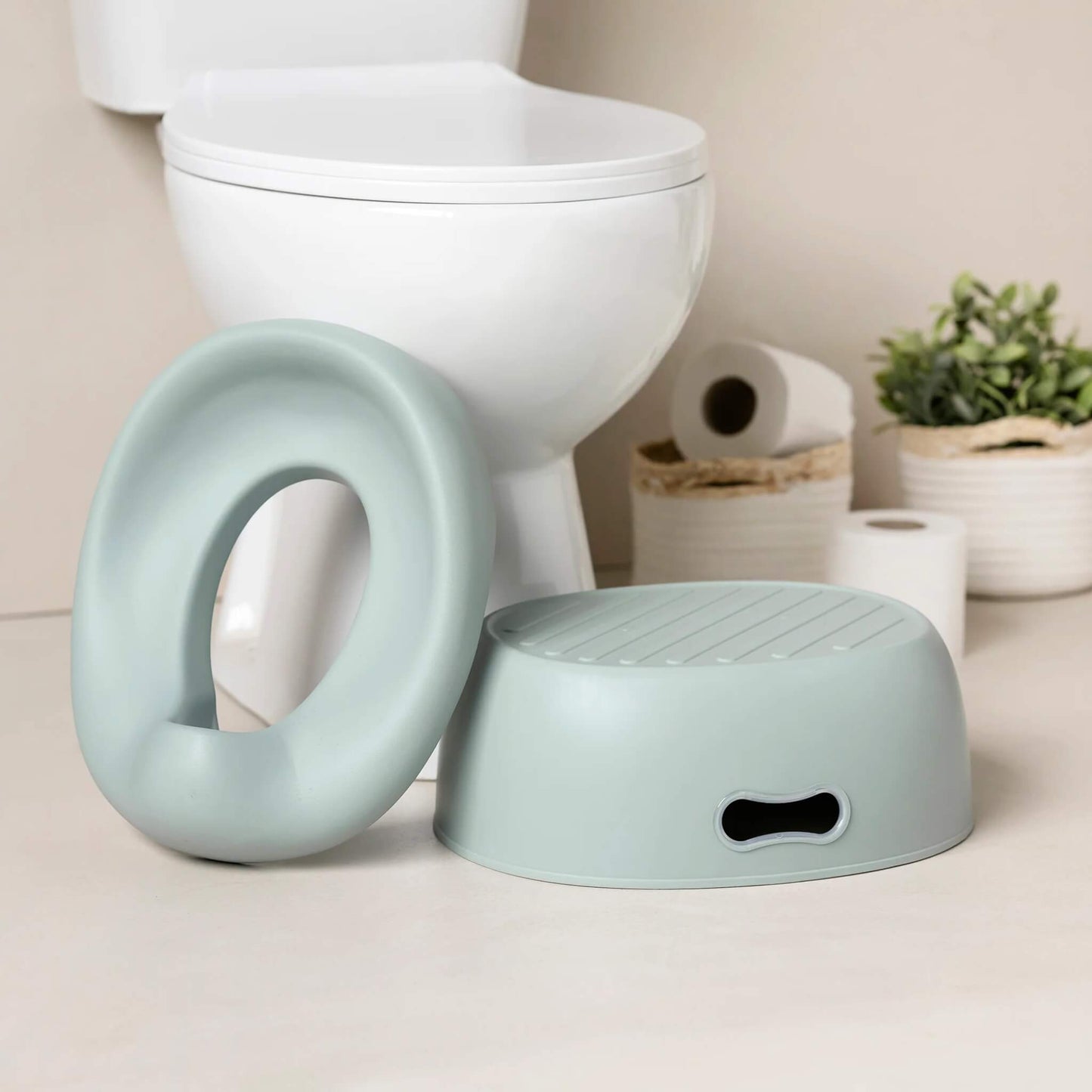A soft green potty seat and a matching step stool placed on a bathroom floor next to a white toilet.