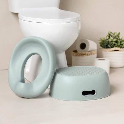 A soft green potty seat and a matching step stool placed on a bathroom floor next to a white toilet.