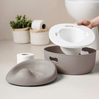 A bathroom scene with a taupe potty as the inner bowl is being lifted out of the base while the cushioned seat lies nearby.