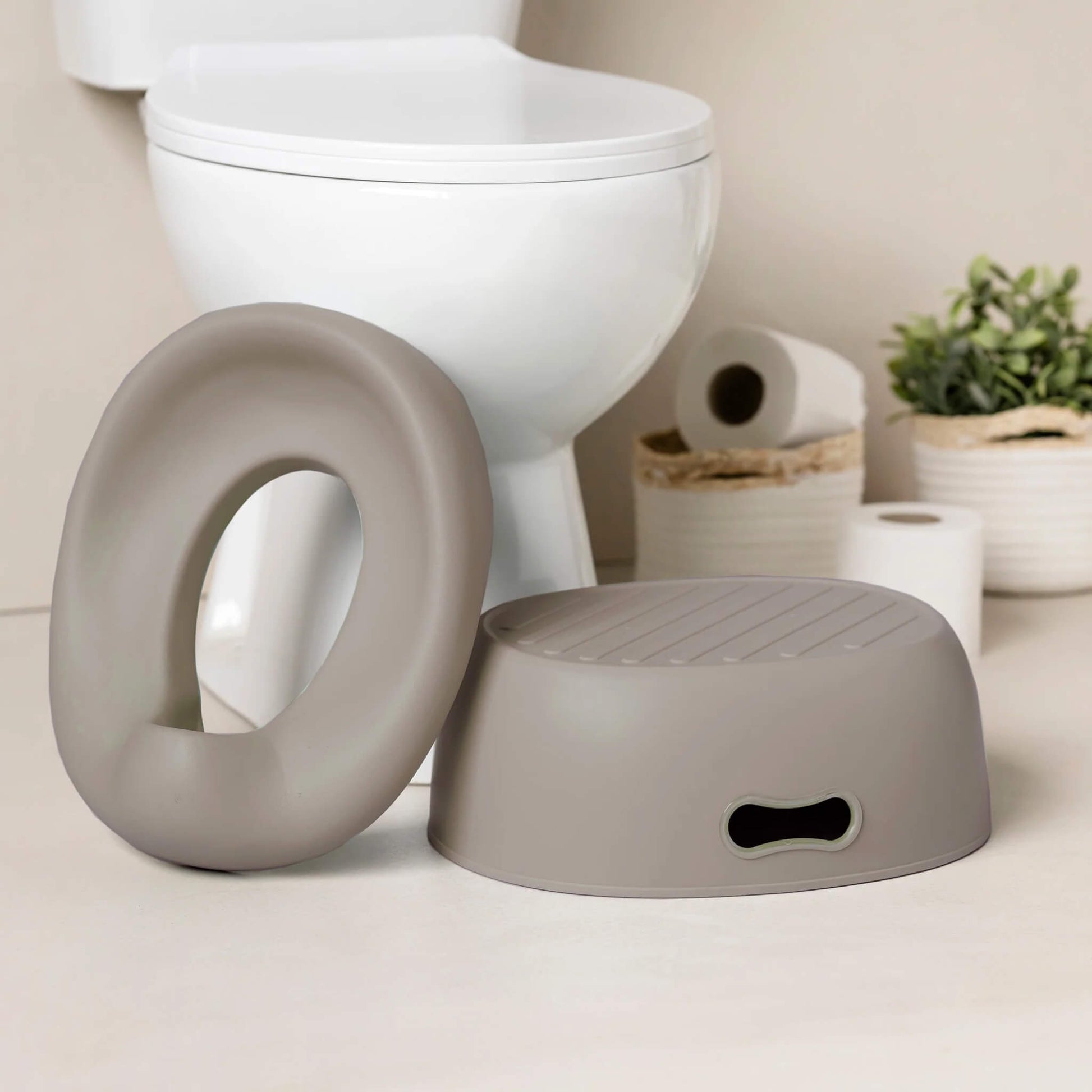 A taupe potty seat and a matching step stool placed on the bathroom floor next to a white toilet.