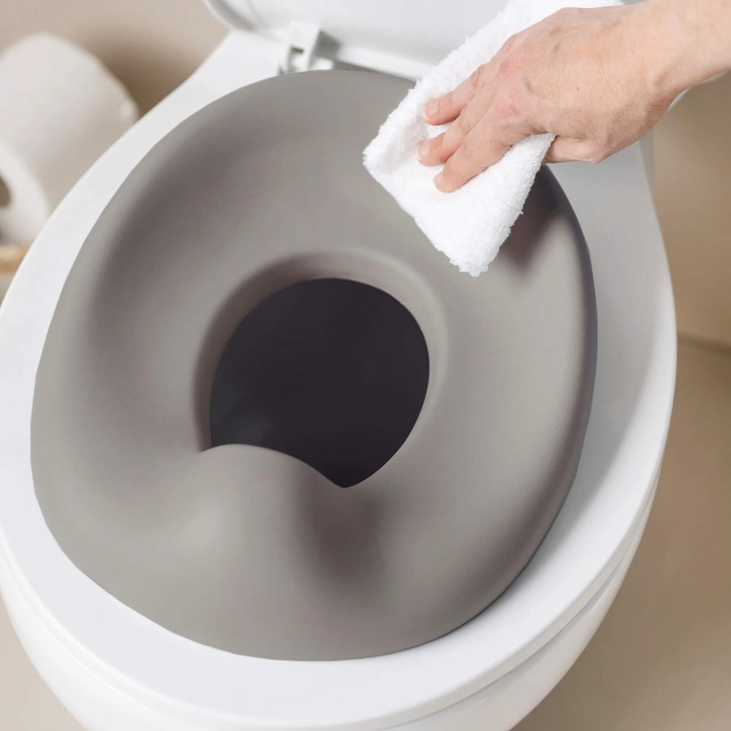 A hand wiping a taupe potty seat while it sits on a toilet, showing the smooth, easy-clean surface.