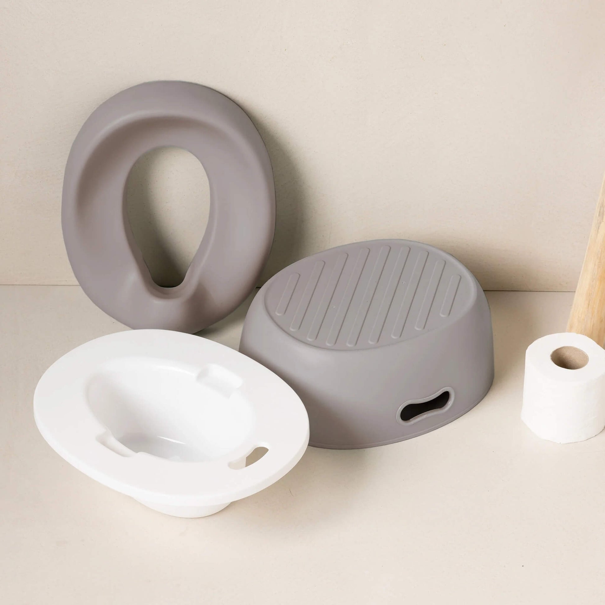 A set of taupe potty components on a bathroom surface, including a cushioned seat, a white inner bowl and a matching step stool.