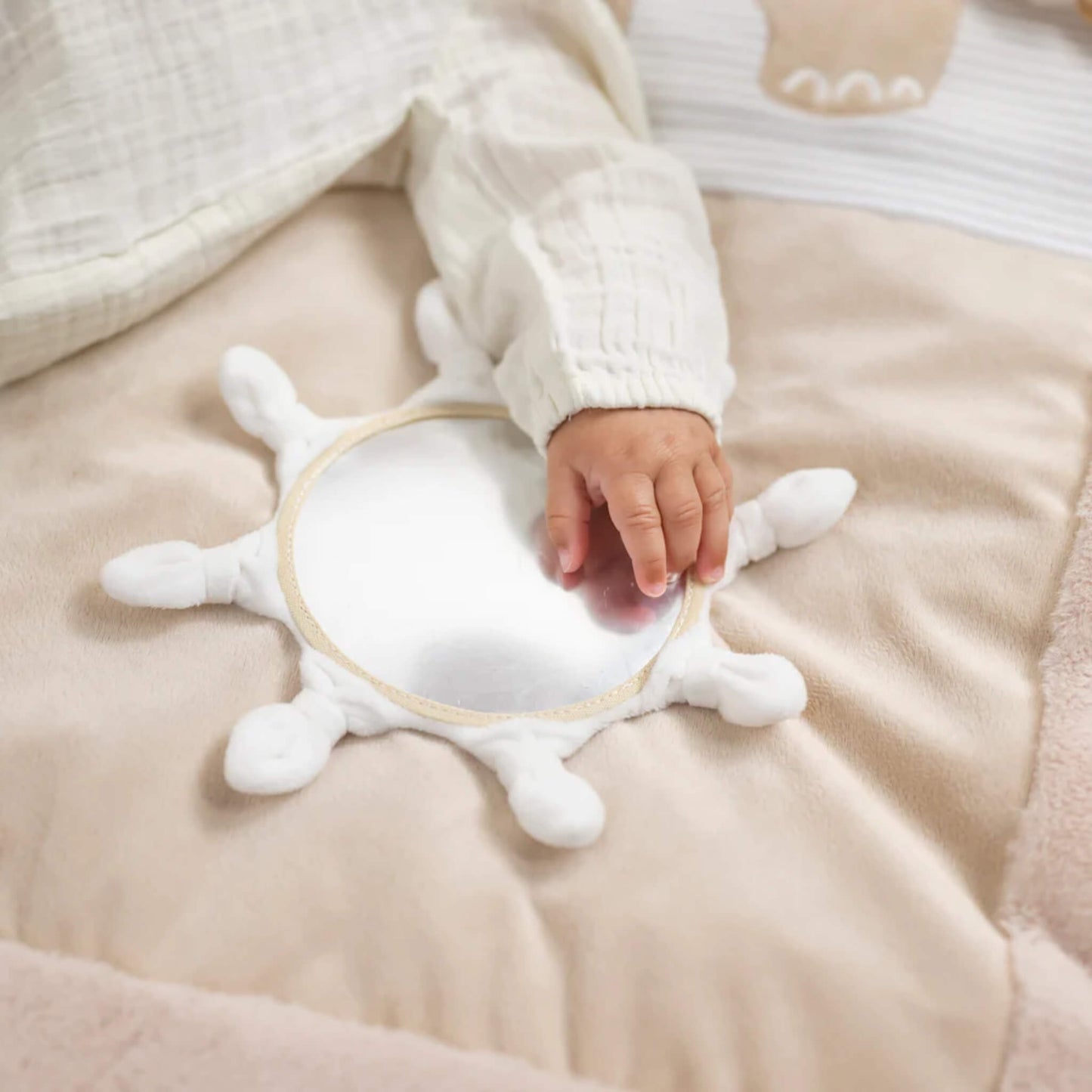 Small hand touching round baby-safe mirror sewn into cushioned playmat surface for sensory exploration.