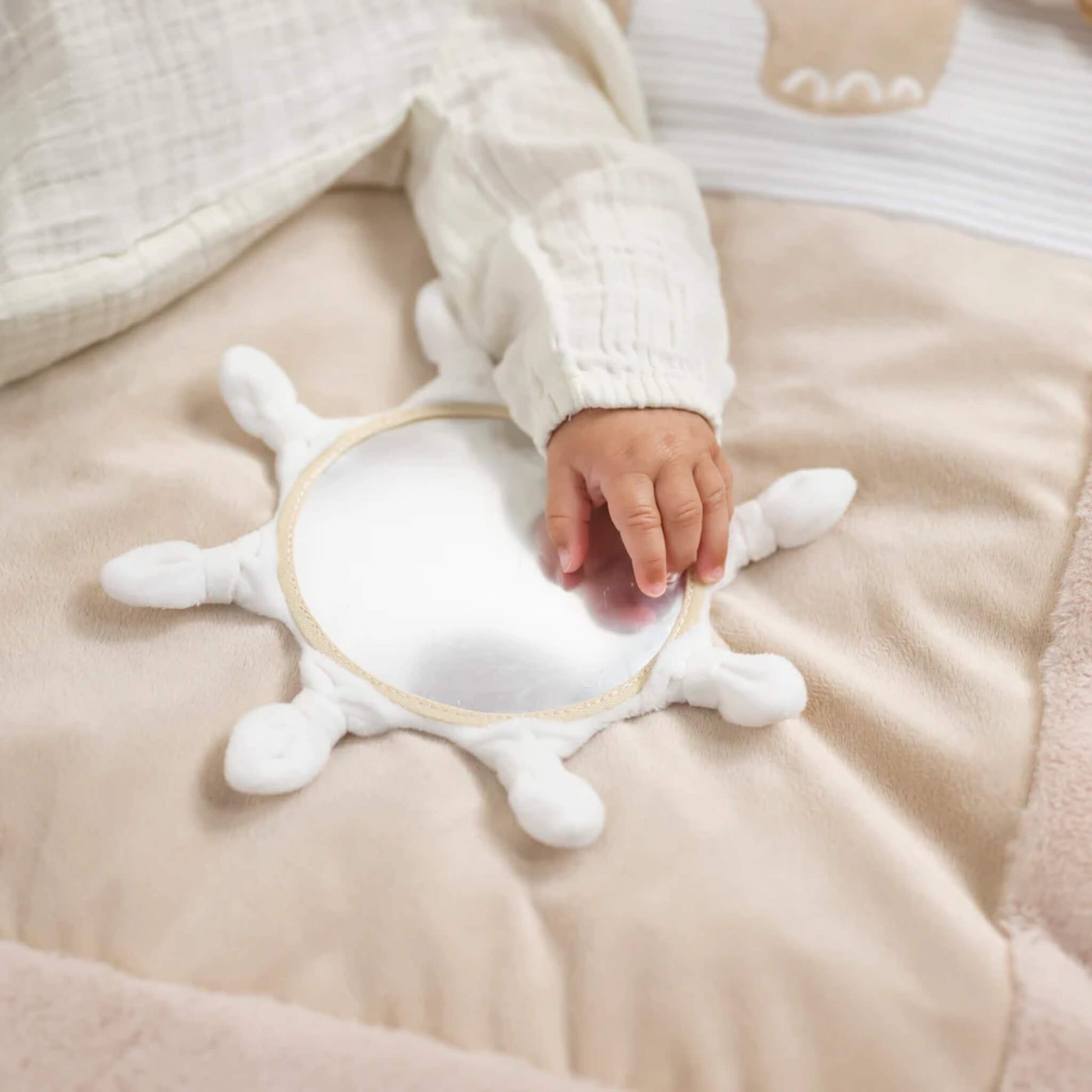 Small hand touching round baby-safe mirror sewn into cushioned playmat surface for sensory exploration.