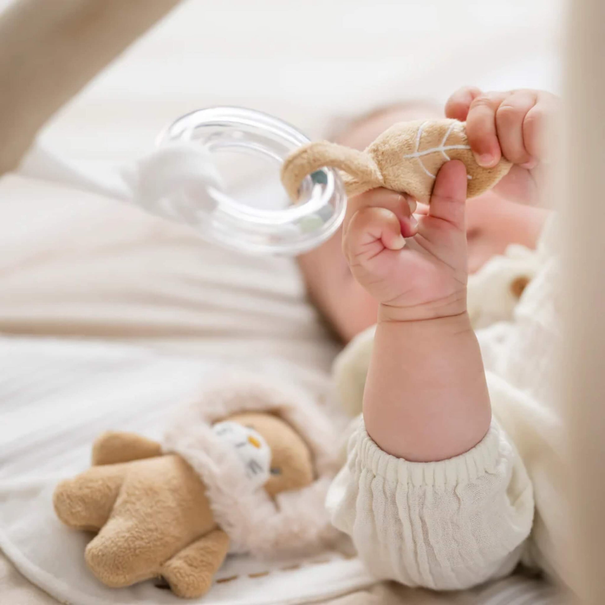 Baby gripping soft fabric rattle with clear ring and textured cloth tabs designed for grasping and fine motor practice.