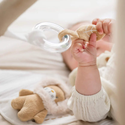 Baby gripping soft fabric rattle with clear ring and textured cloth tabs designed for grasping and fine motor practice.