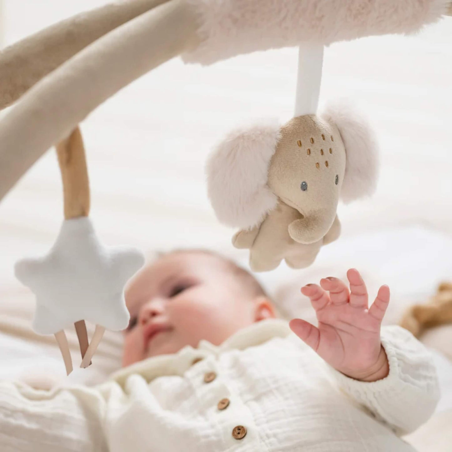 Close view of plush hanging elephant toy attached to fabric arch above baby during tummy time play.