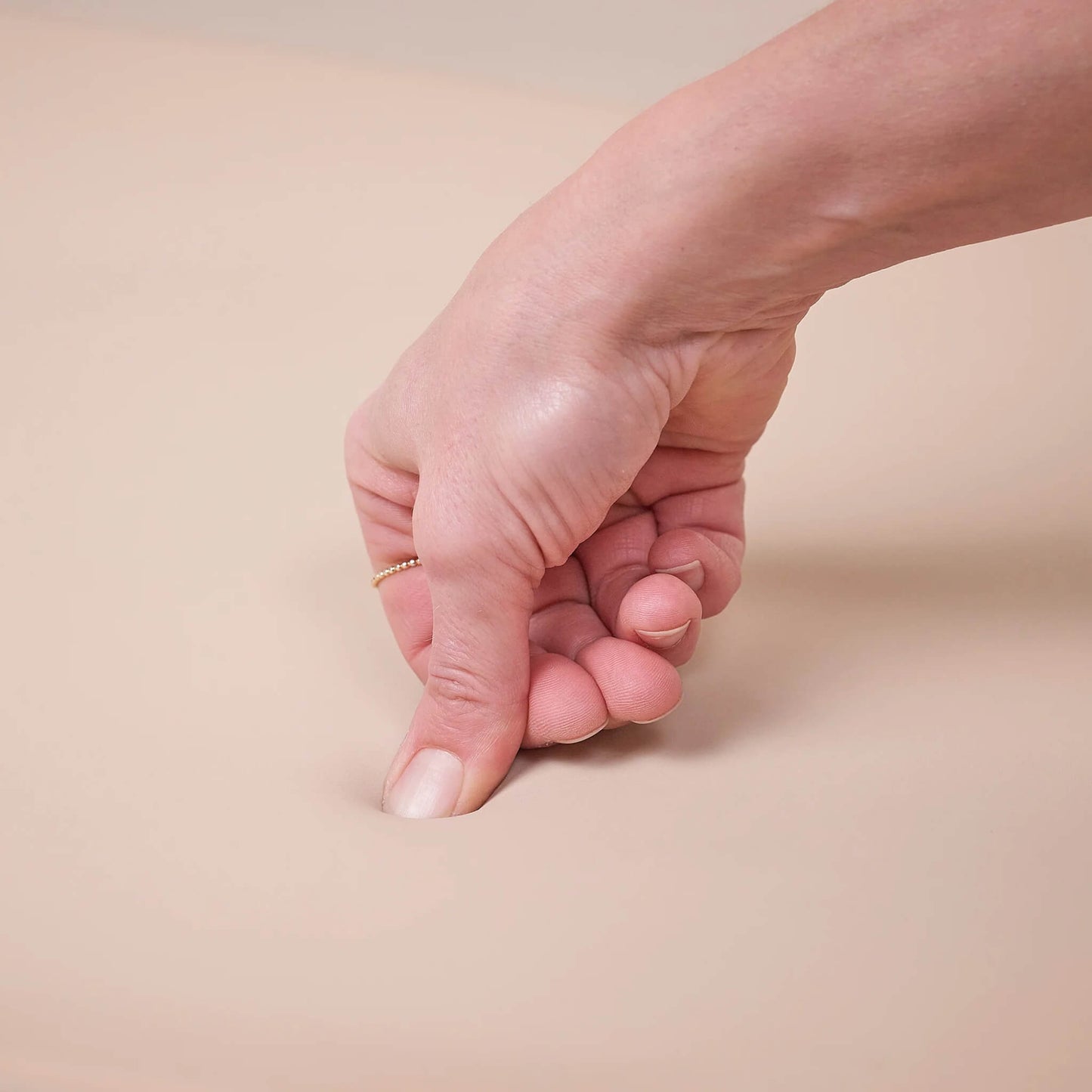 Close-up of an adult’s hand gently pressing into the soft surface of a beige changing pad to show its flexibility.