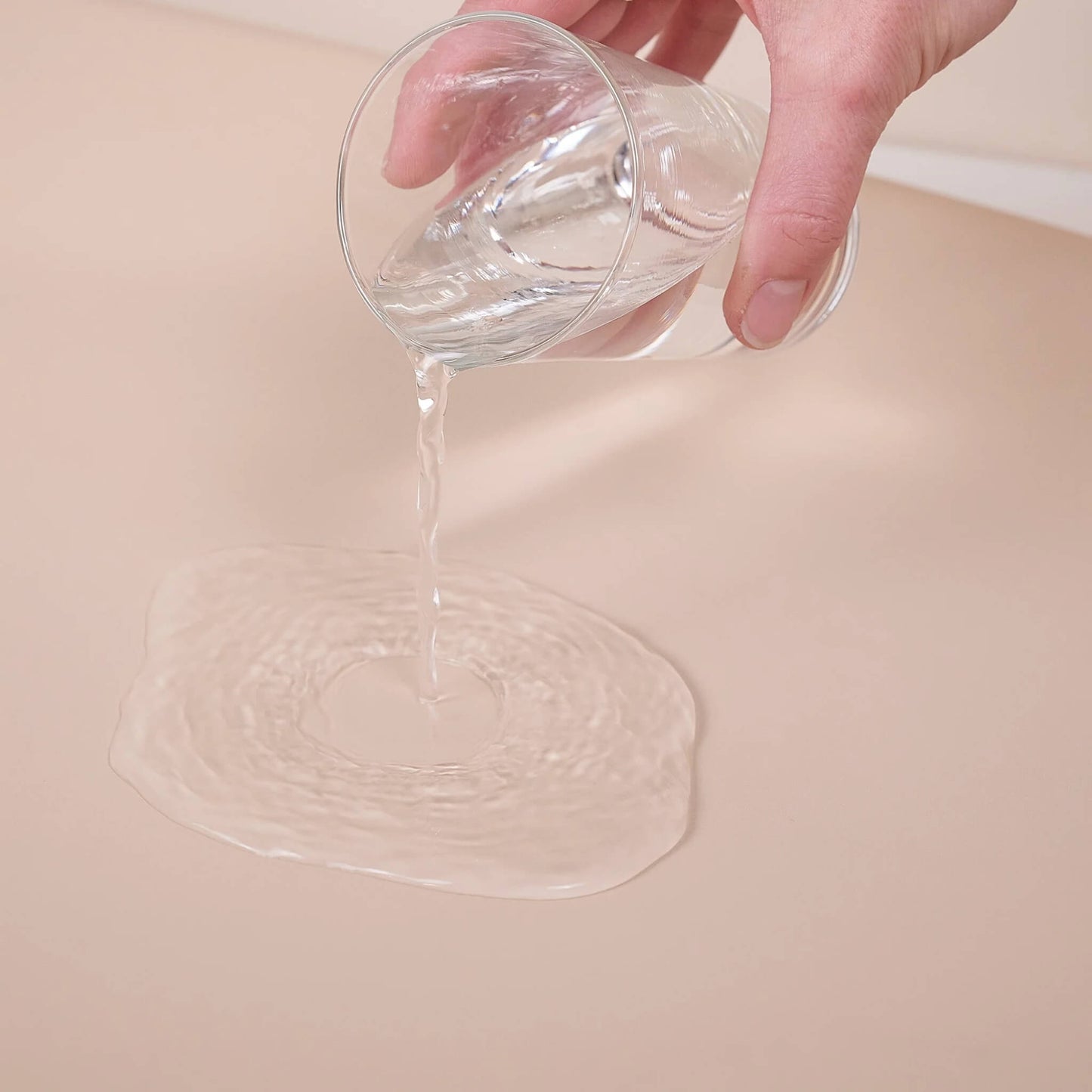 Water being poured onto the surface of a beige changing pad to demonstrate its waterproof design.