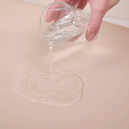 Water being poured onto the surface of a beige changing pad to demonstrate its waterproof design.