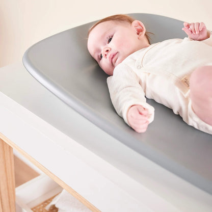 Baby lying on a grey changing pad with their head resting on the curved surface and body relaxed.