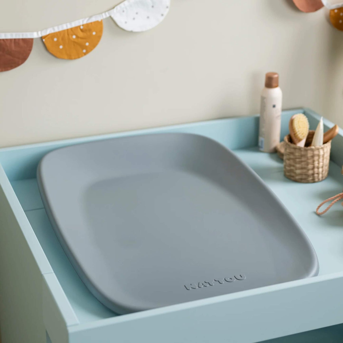 Grey changing pad placed inside a light blue changing unit with baby care items arranged nearby.