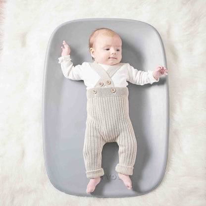 Baby lying on a grey changing pad placed on a soft, fluffy surface, arms and legs gently extended.