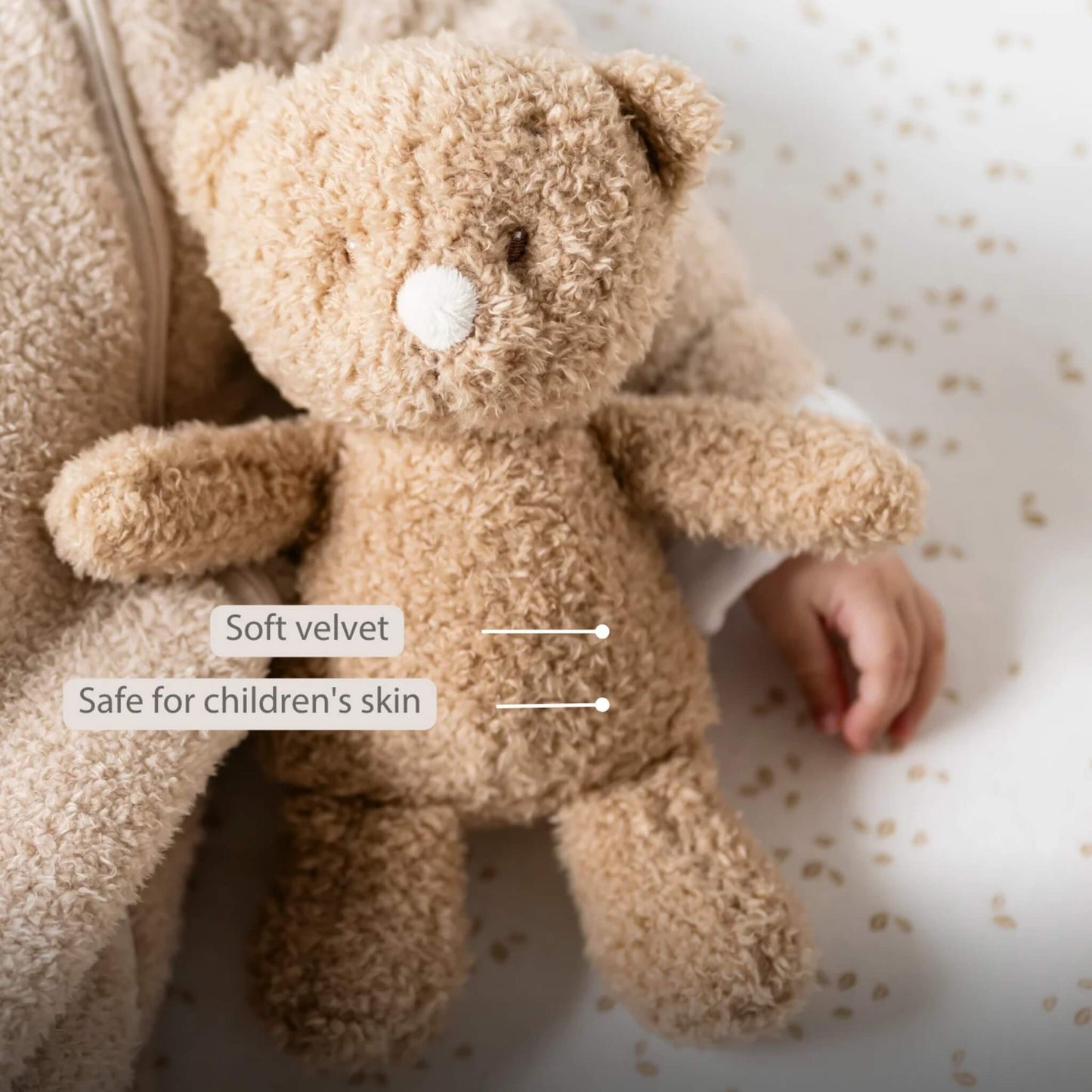 Close-up of a beige teddy bear lying beside a baby, showing soft textured fur and simple stitched features with the text ‘Soft velvet’ and ‘Safe for children’s skin’ on the image.