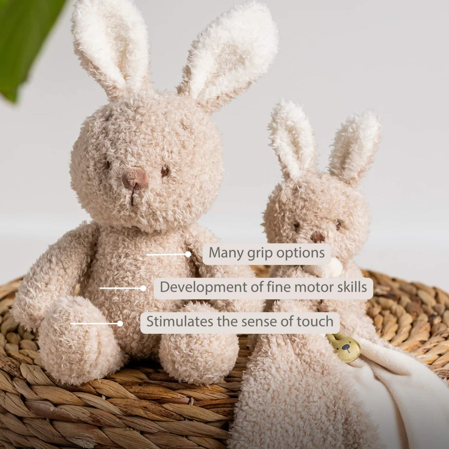 A plush bunny sitting beside a matching comforter on a woven basket, with labels highlighting grip options, fine motor development and tactile stimulation.