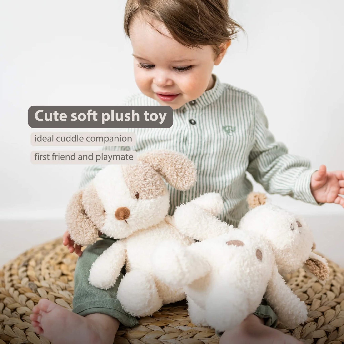 A small child sitting on a woven mat while holding a fluffy dog soft toy, with another similar toy resting beside them.