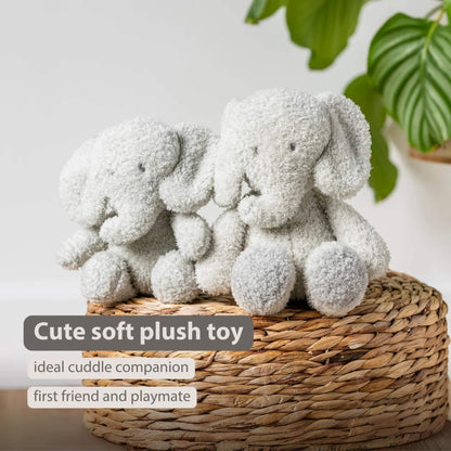 A pair of soft plush elephant toys sitting on a woven basket, both facing forward with rounded limbs and textured fur. The words “Cute soft plush toy”, “ideal cuddle companion” and “first friend and playmate” appear on the image.